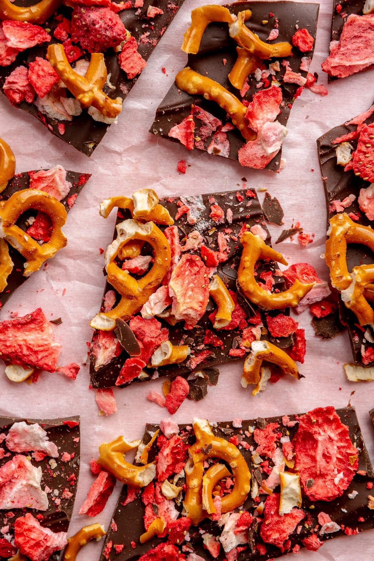 Dark chocolate bark with strawberries and pretzels sits on a light pink paper background.