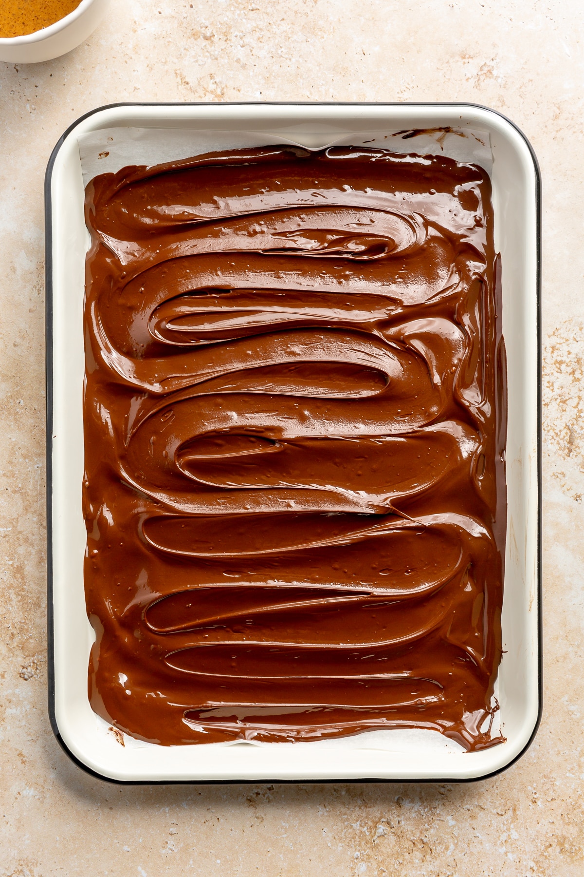 Melted chocolate has been spread in an even layer over the entire parchment lined baking tray.