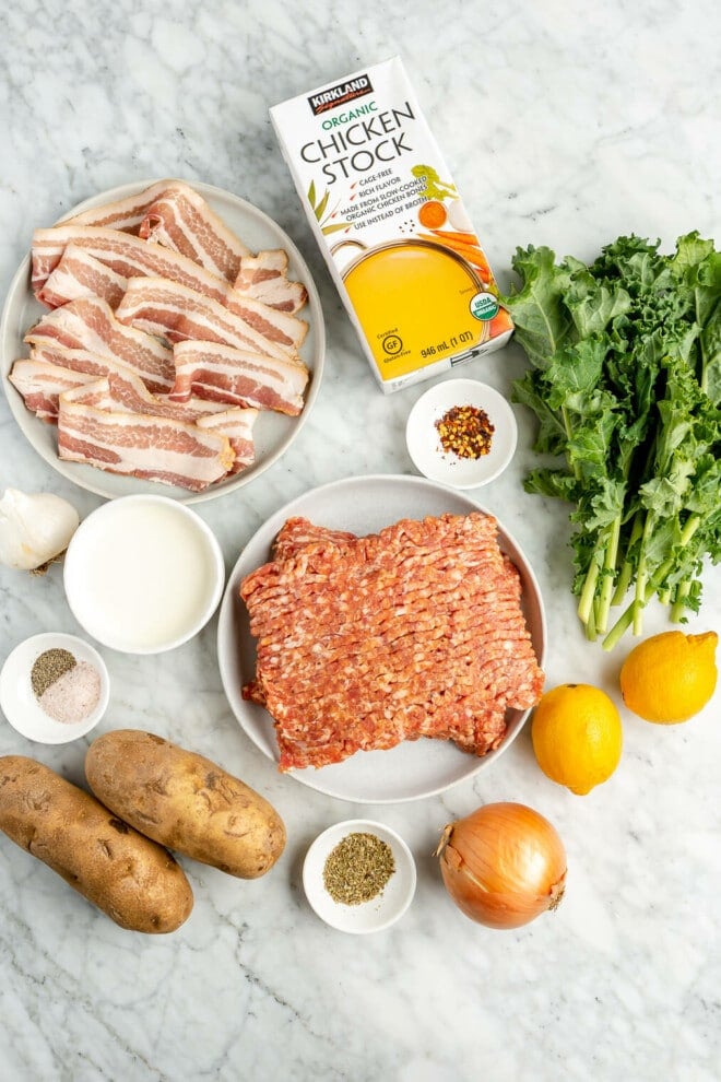 Ingredients needed for creamy kale and sausage soup (zuppa toscana) on a marble countertop.
