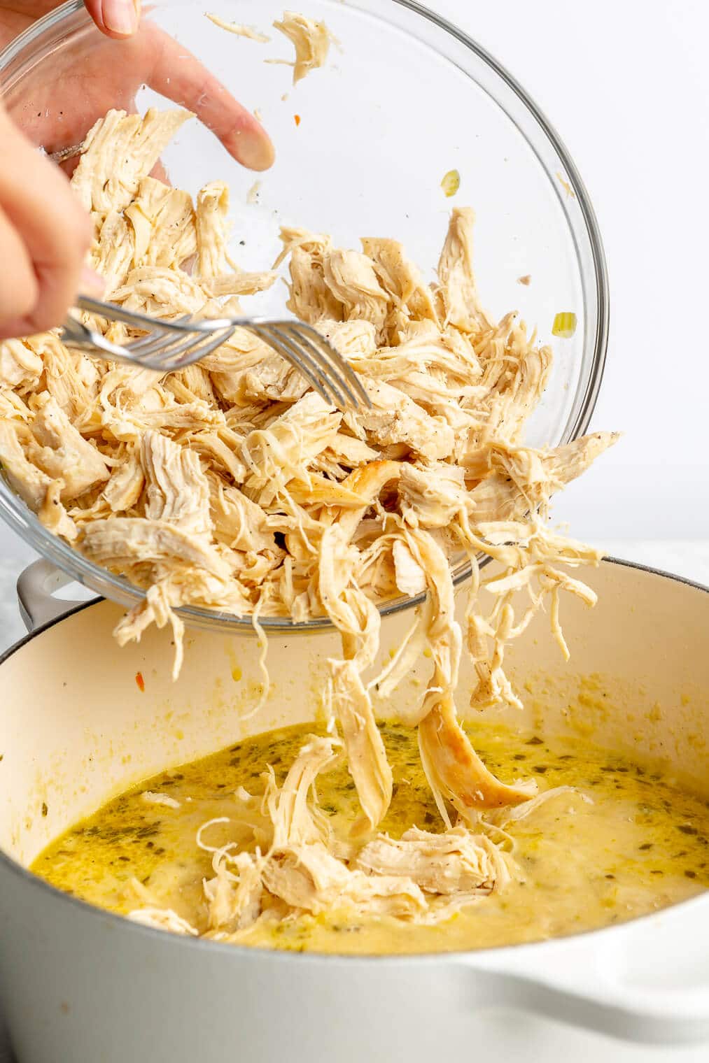 A person adding shredded chicken into a large pot of chicken and dumplings.