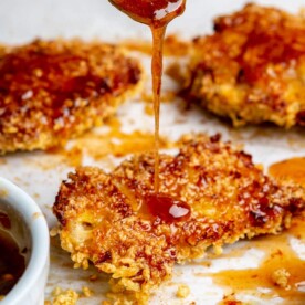 A person drizzling hot honey sauce over crispy hot honey chicken thighs.