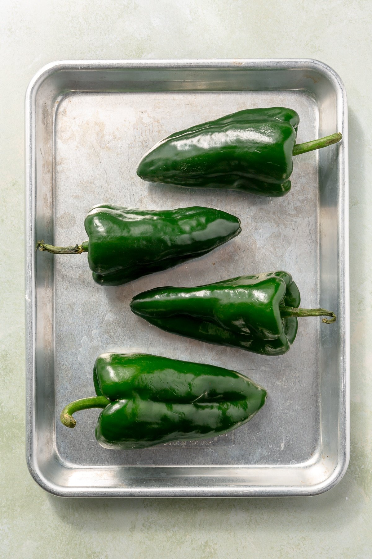 4 green peppers sit on a metal tray.