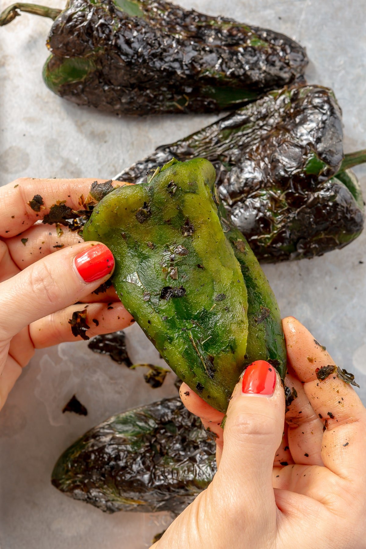 2 hands are shown removing the charring from the green peppers.