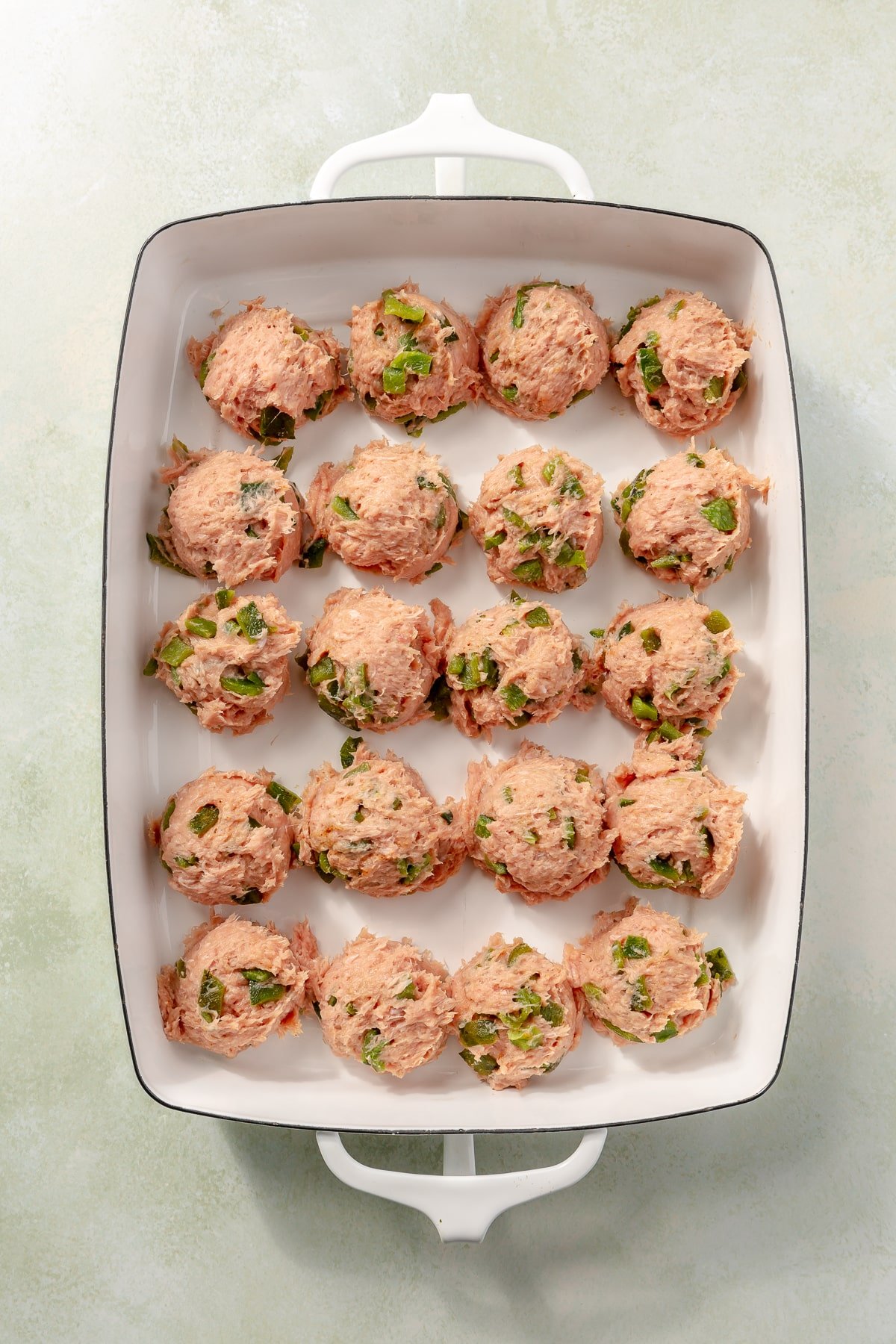 Balls of turkey meatball mixture sit in a white baking tray.