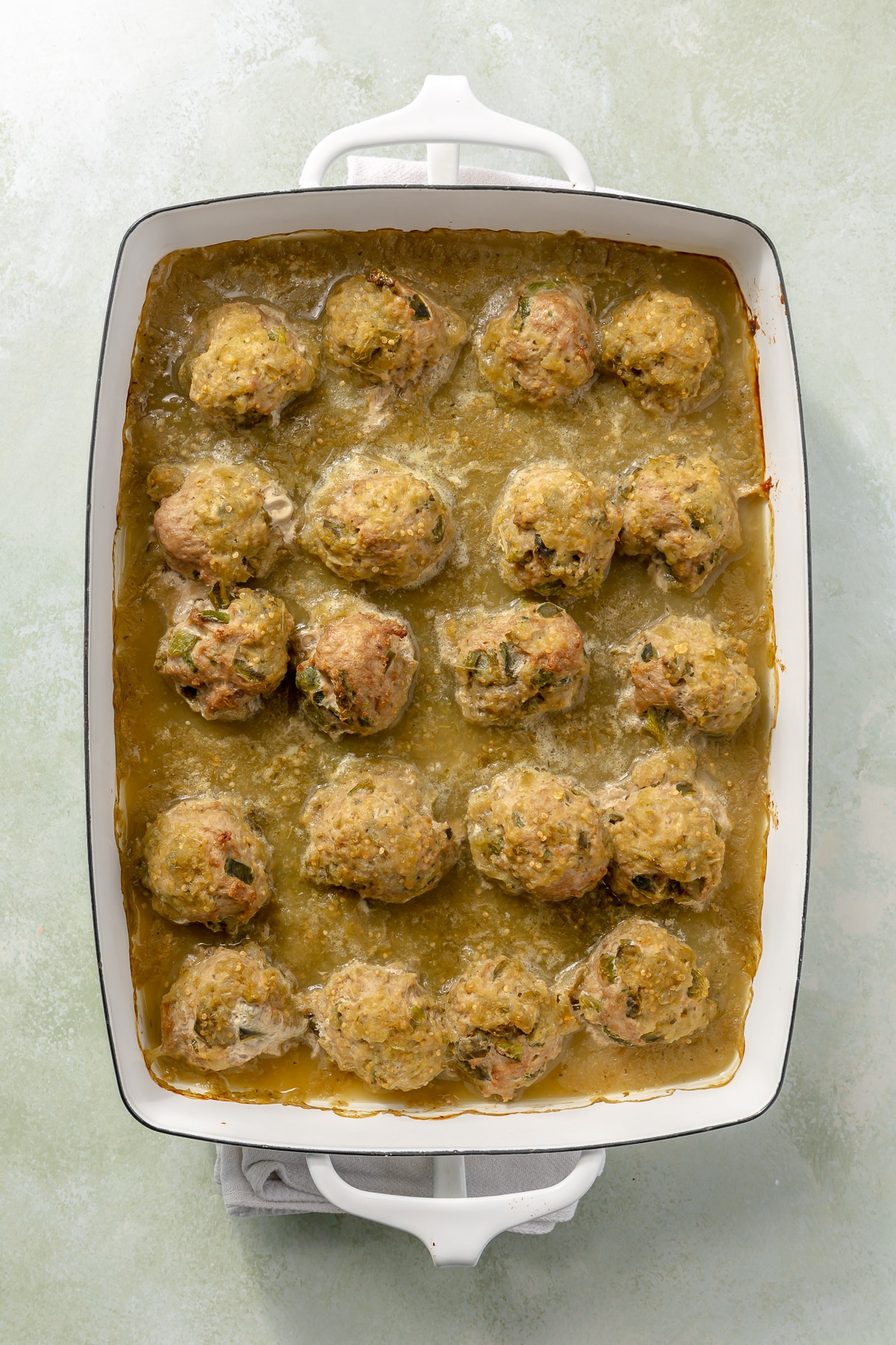 A green sauce has been poured over the top. of the meatballs.