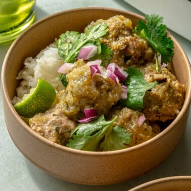 Enchilada verde turkey meatballs have been served in two bowls over white rice. Diced onions and cilantro have been placed on top for garnish.