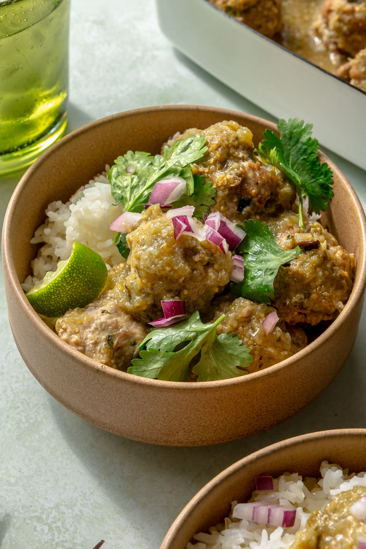 Enchilada verde turkey meatballs have been served in two bowls over white rice. Diced onions and cilantro have been placed on top for garnish.