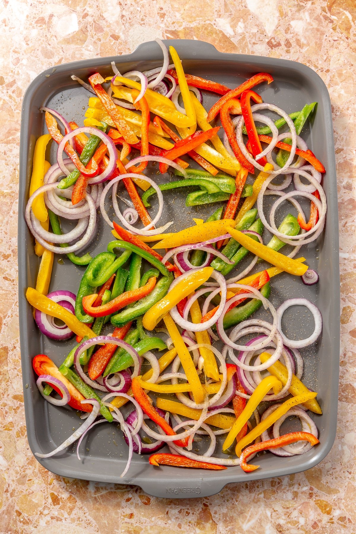 Chopped red, yellow, and orange bell peppers and sliced purple onion sit on a baking tray.
