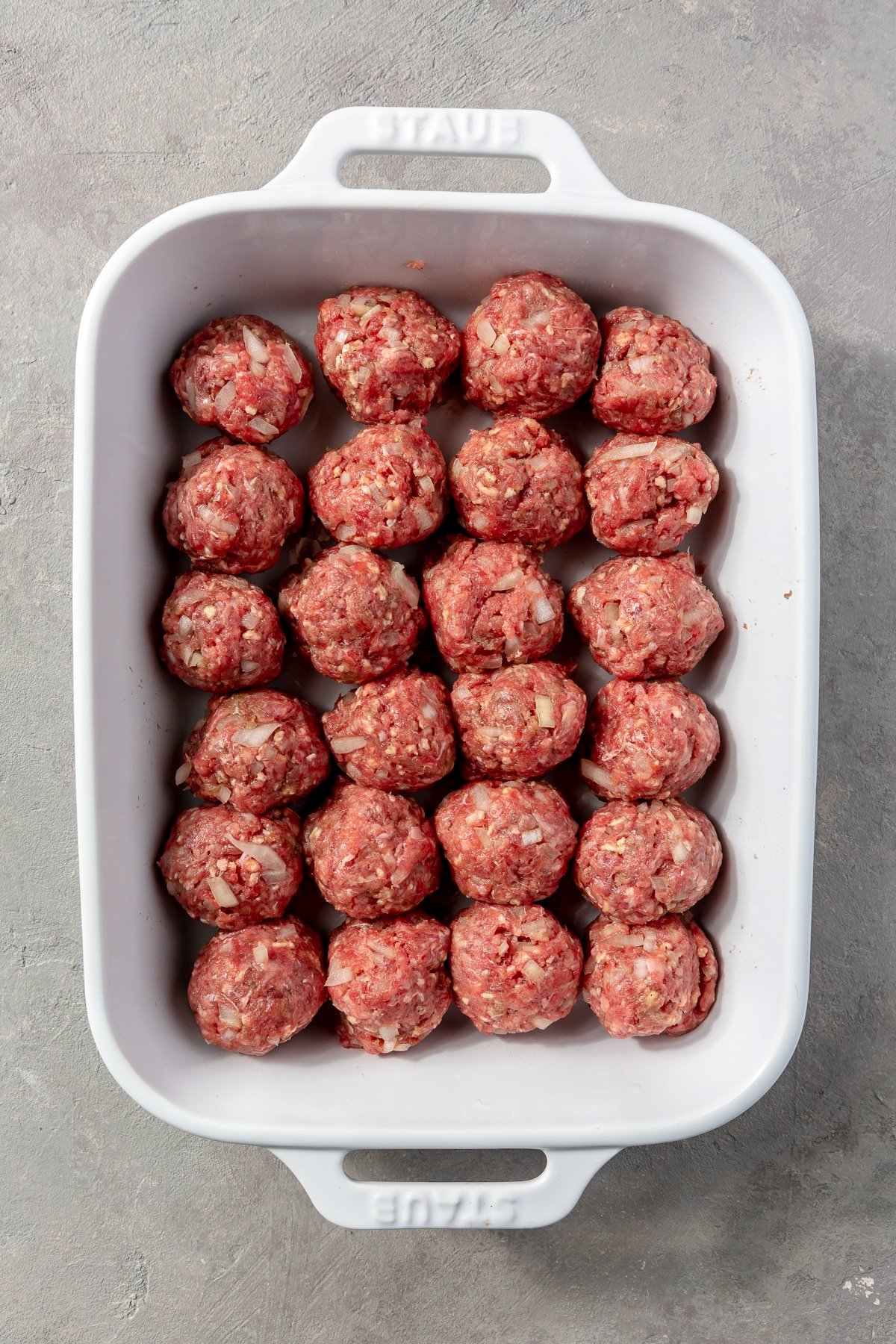 1 inch round meatballs fill the bottom of a white baking dish.