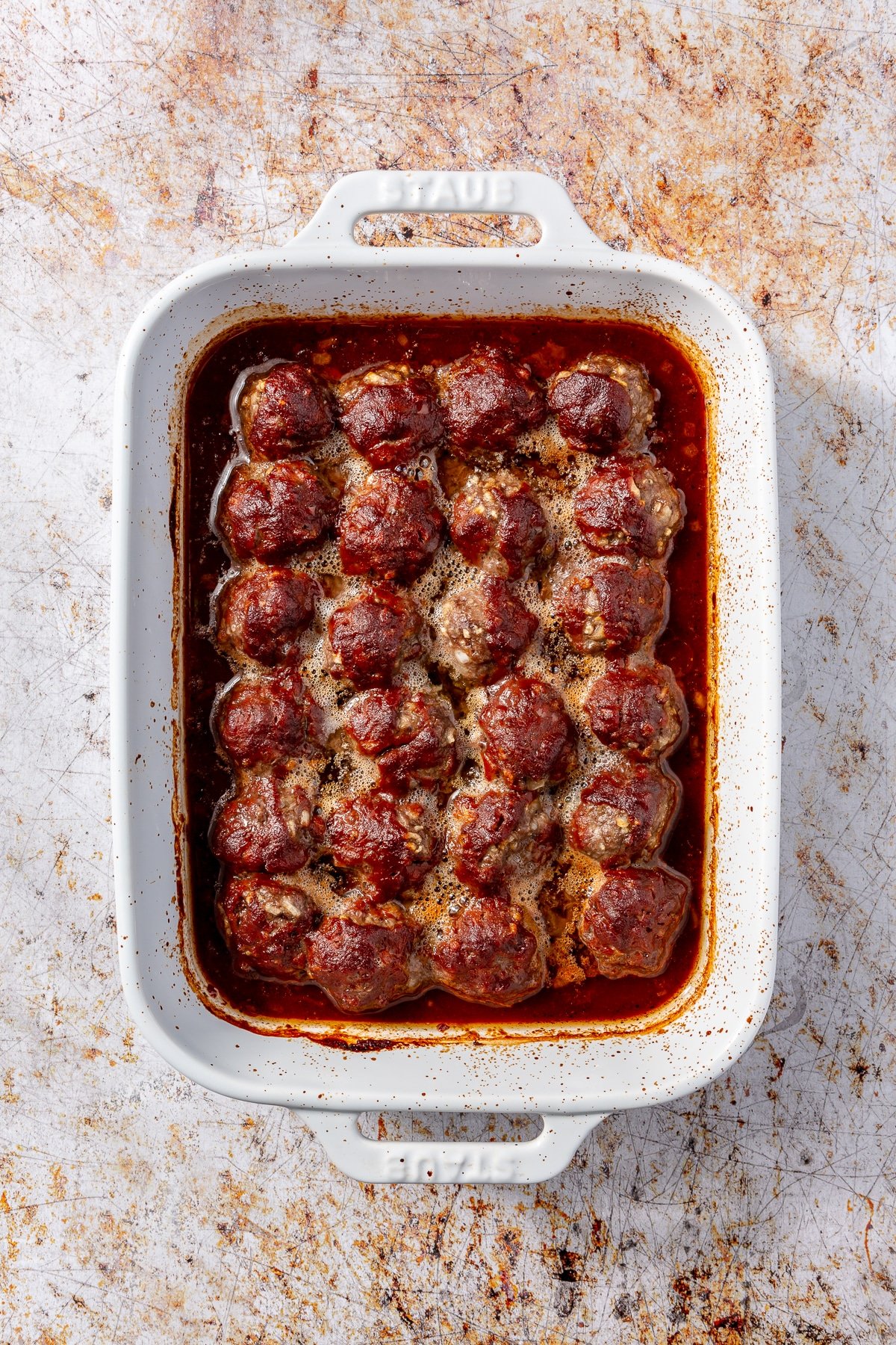 Fully baked meatballs with sauce sit in a white baking dish.