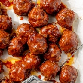 The finished bbq meatballs have been served on a parchment paper covered serving tray. The remaining sauce sits in a bowl to the side.