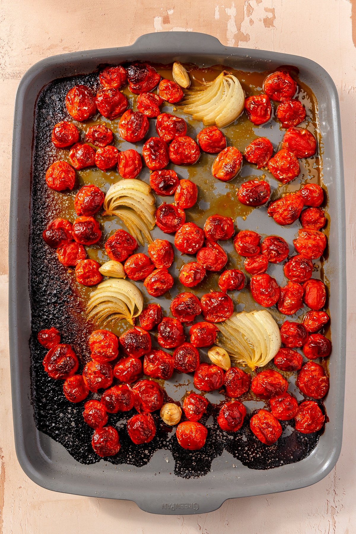 Fully baked tomatoes and onion sit on a metal baking tray.