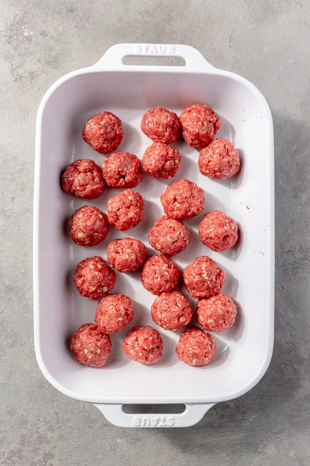 The ground beef mixture has been rolled into meatballs of which sit in a white baking dish.