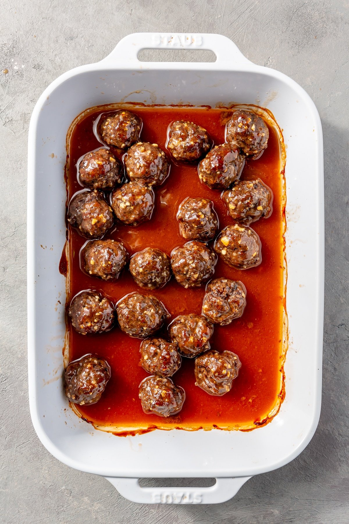 Fully baked meatballs sit in a white baking dish.