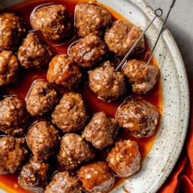 Sweet and sour meatballs have been placed in a serving bowl. Serving skewers have been placed in a couple.