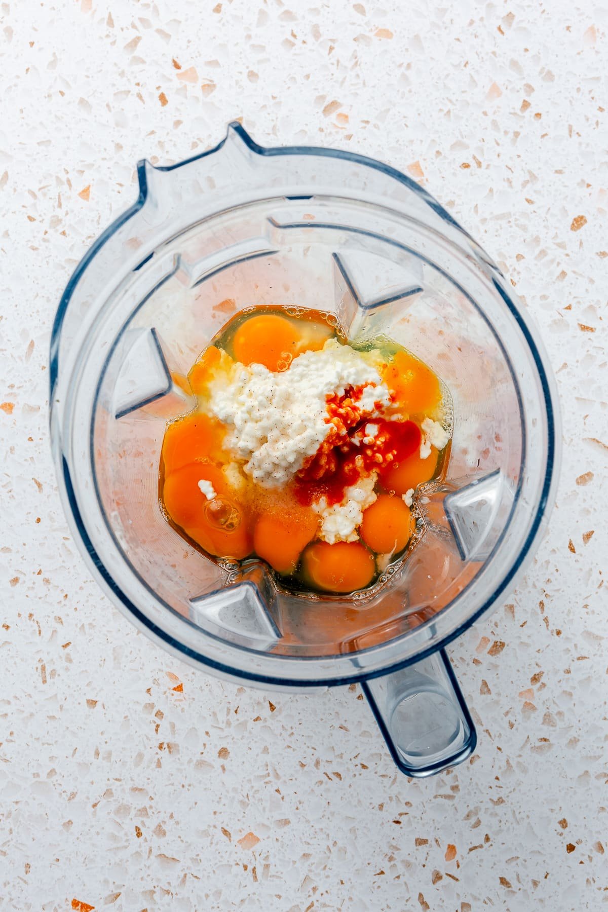 Cracked eggs and a variety of other ingredients have been placed into a blender