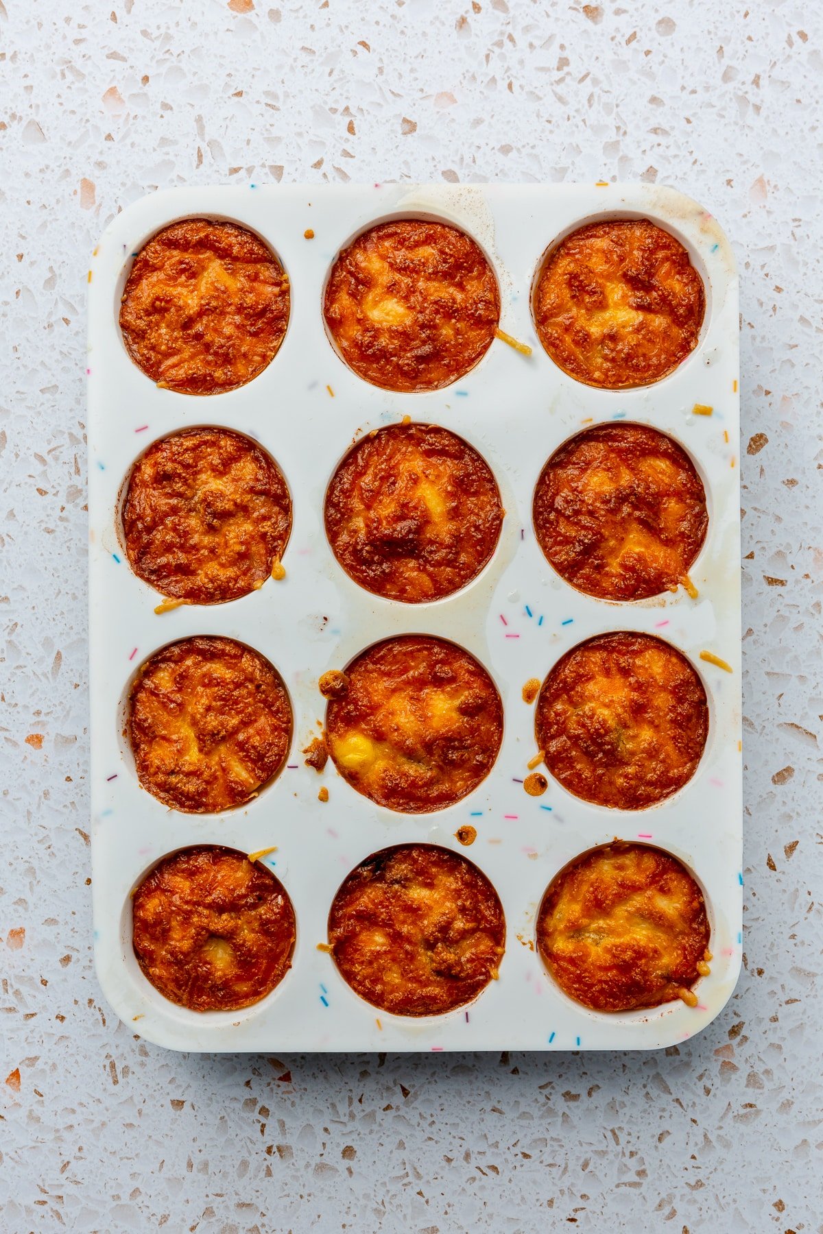 Fully baked and browned egg bites sit in a white, silicone muffin tray.