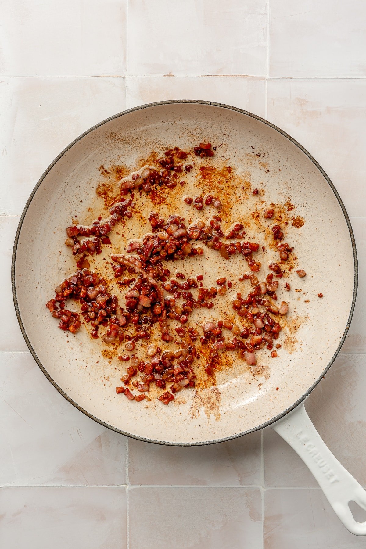 Chopped bacon is shown being cooked in a white frying pan.