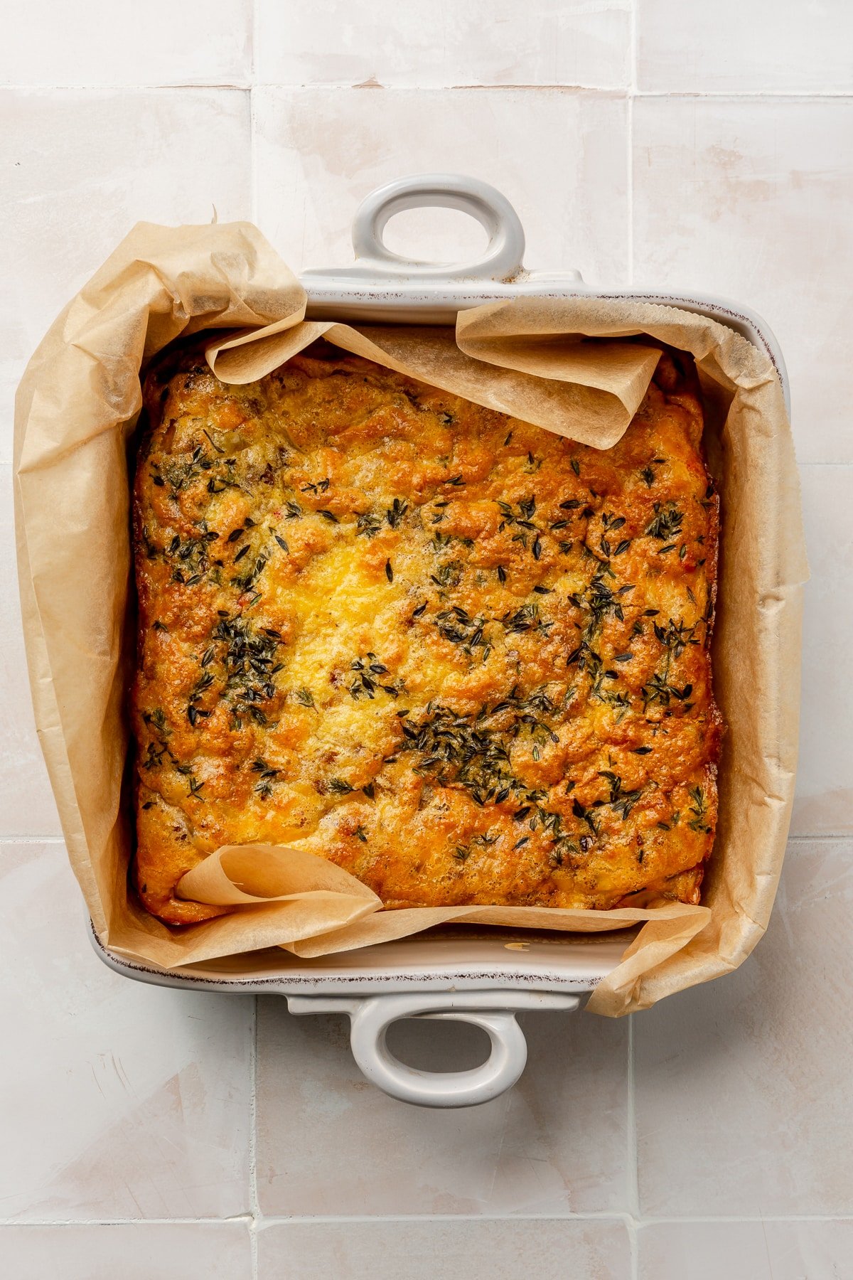 Fully baked crustless quiche Lorraine sits in a parchment lined baking dish.