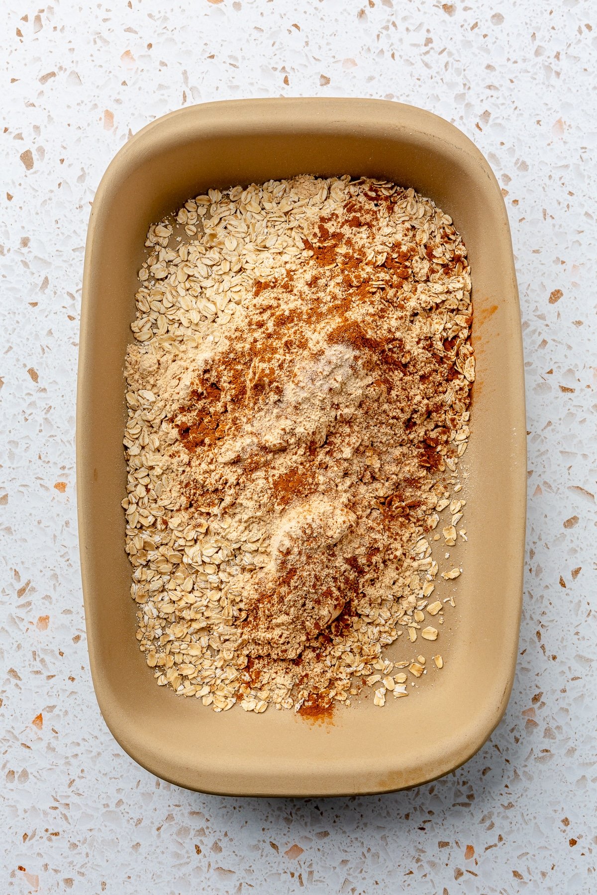 A variety of dry ingredients have been added to a beige-colored baking dish.