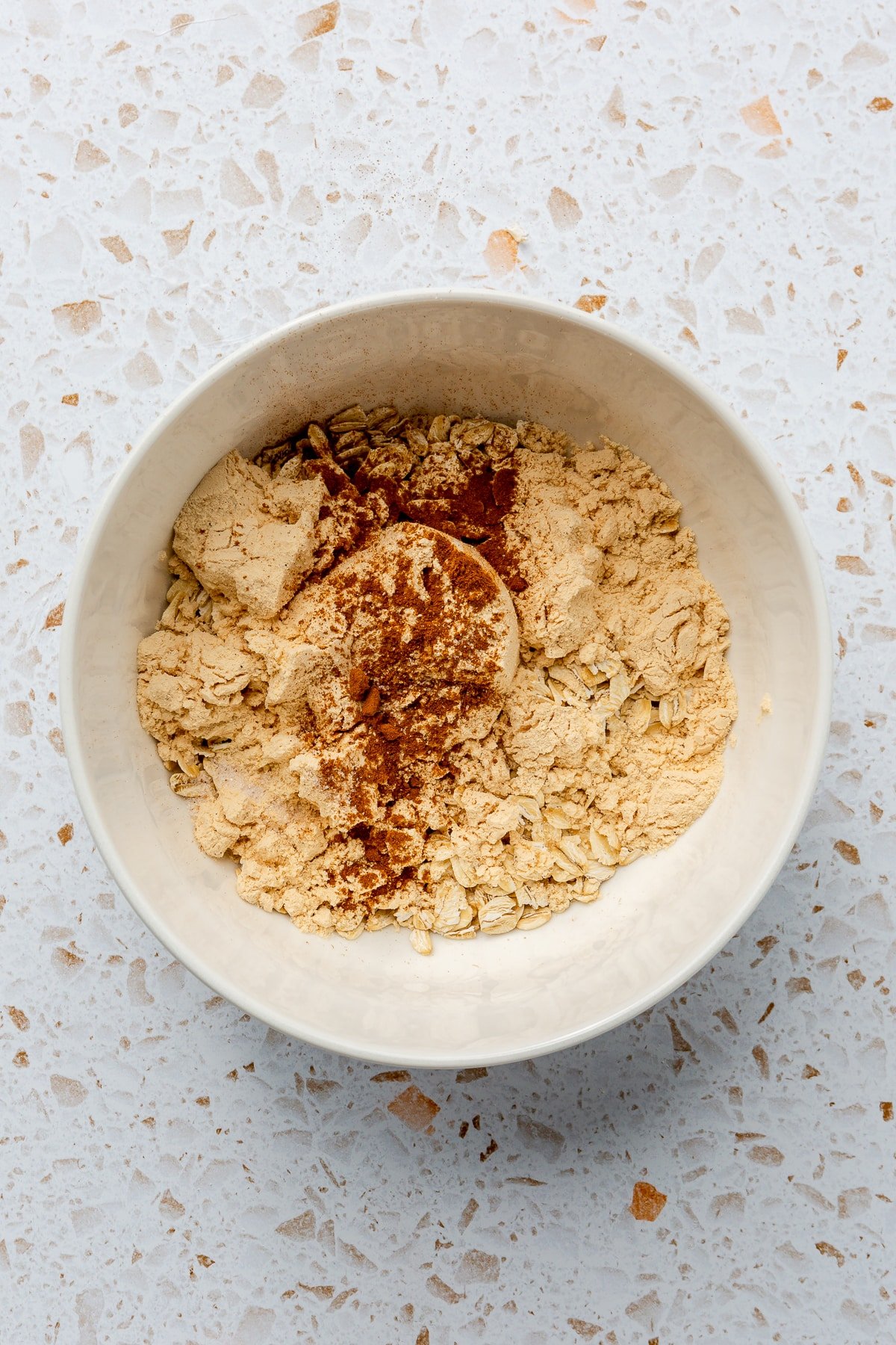 Ingredients for hot protein oatmeal have been placed into a white mixing bowl.