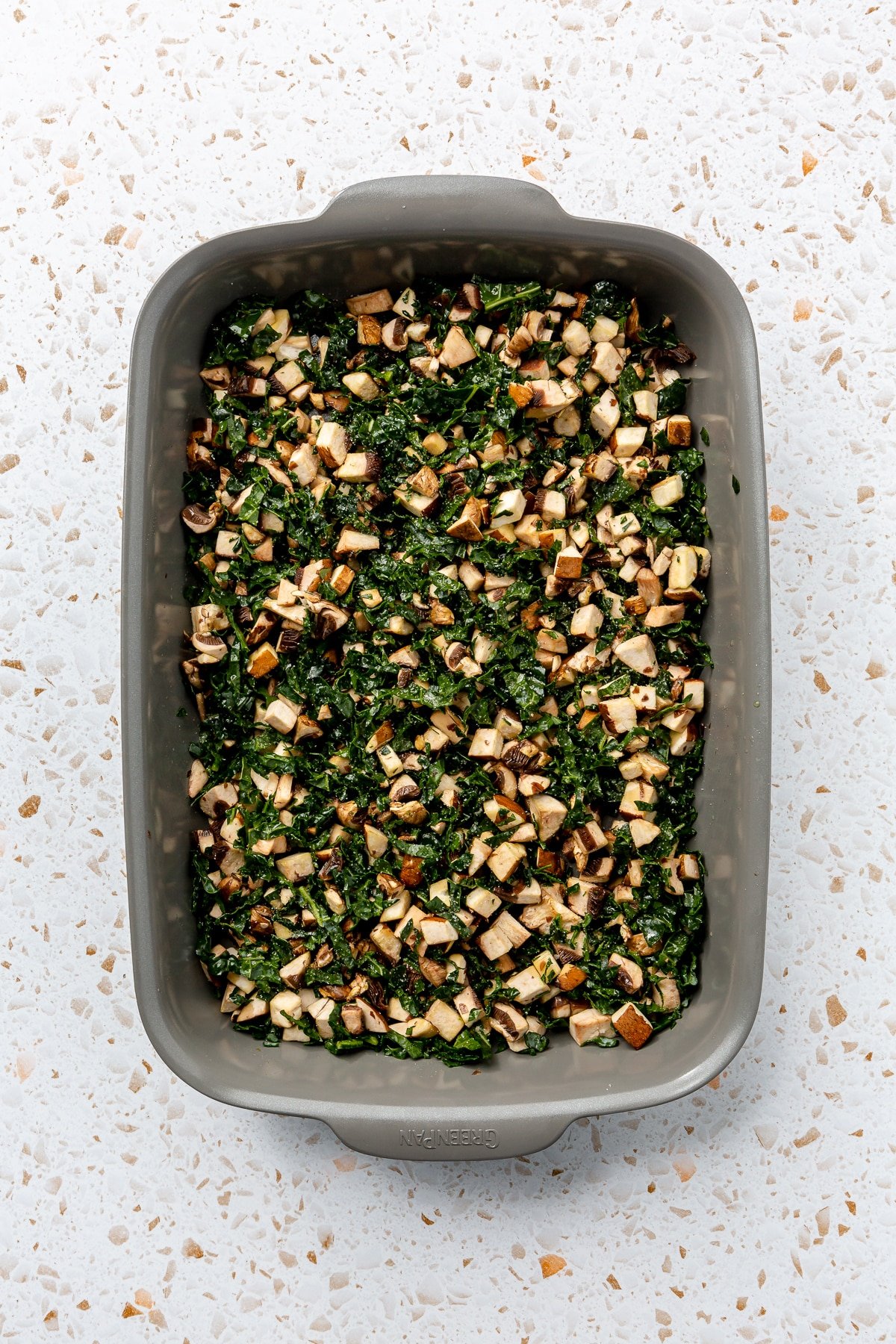 Diced mushrooms and chopped kale have been placed into the bottom of a metal baking dish.