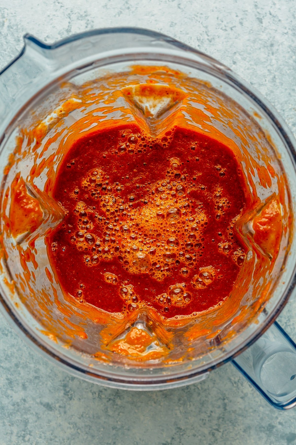 Ingredients have been moved into a blender and been blended to create a bright red saucy mixture.