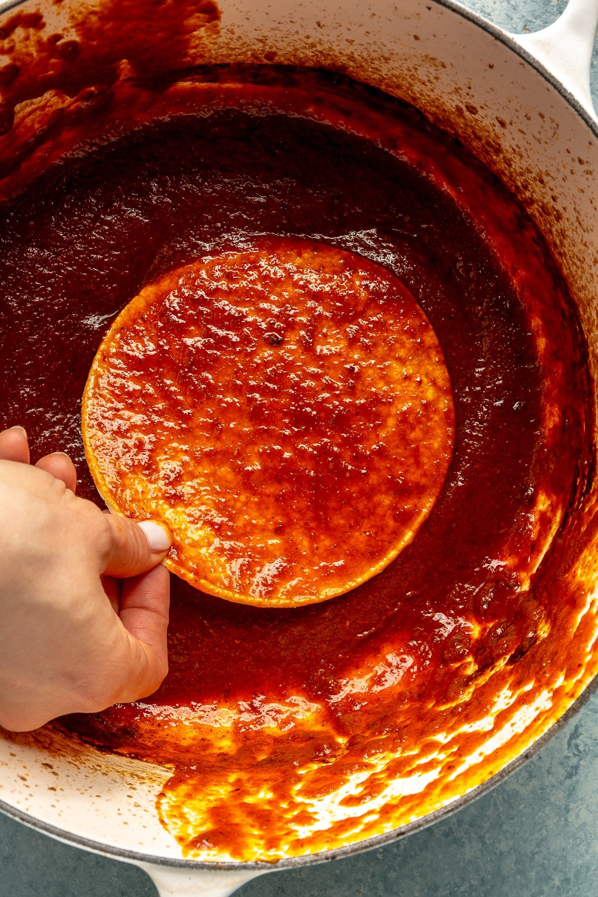 A hand is shown dipping a tortilla into the red sauce.
