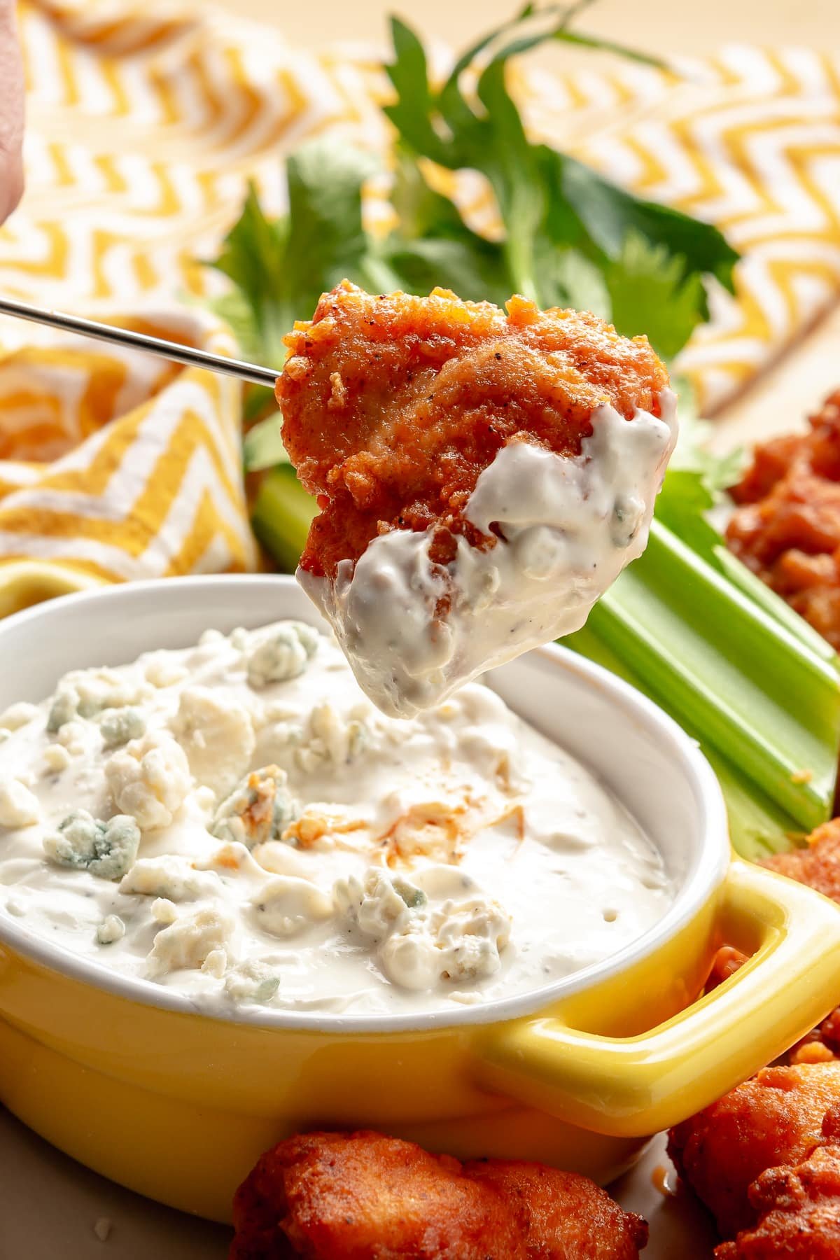 A hand is shown dipping a piece of breaded chicken into the blue cheese dip.
