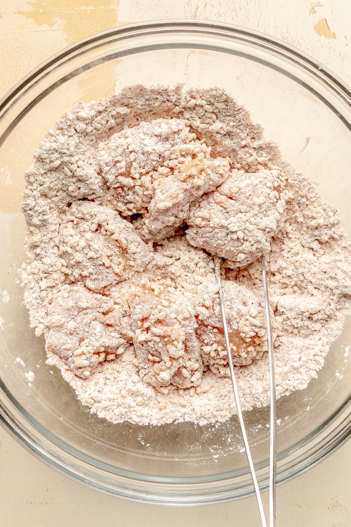 Egg covered chicken pieces are shown being tossed in flour.
