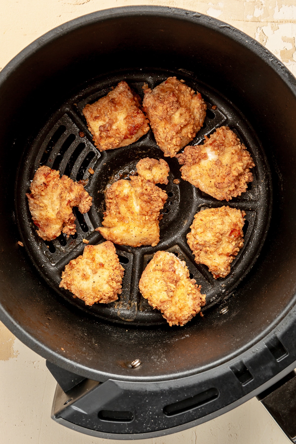 Fully cooked and breaded chicken pieces sit in an air fryer.