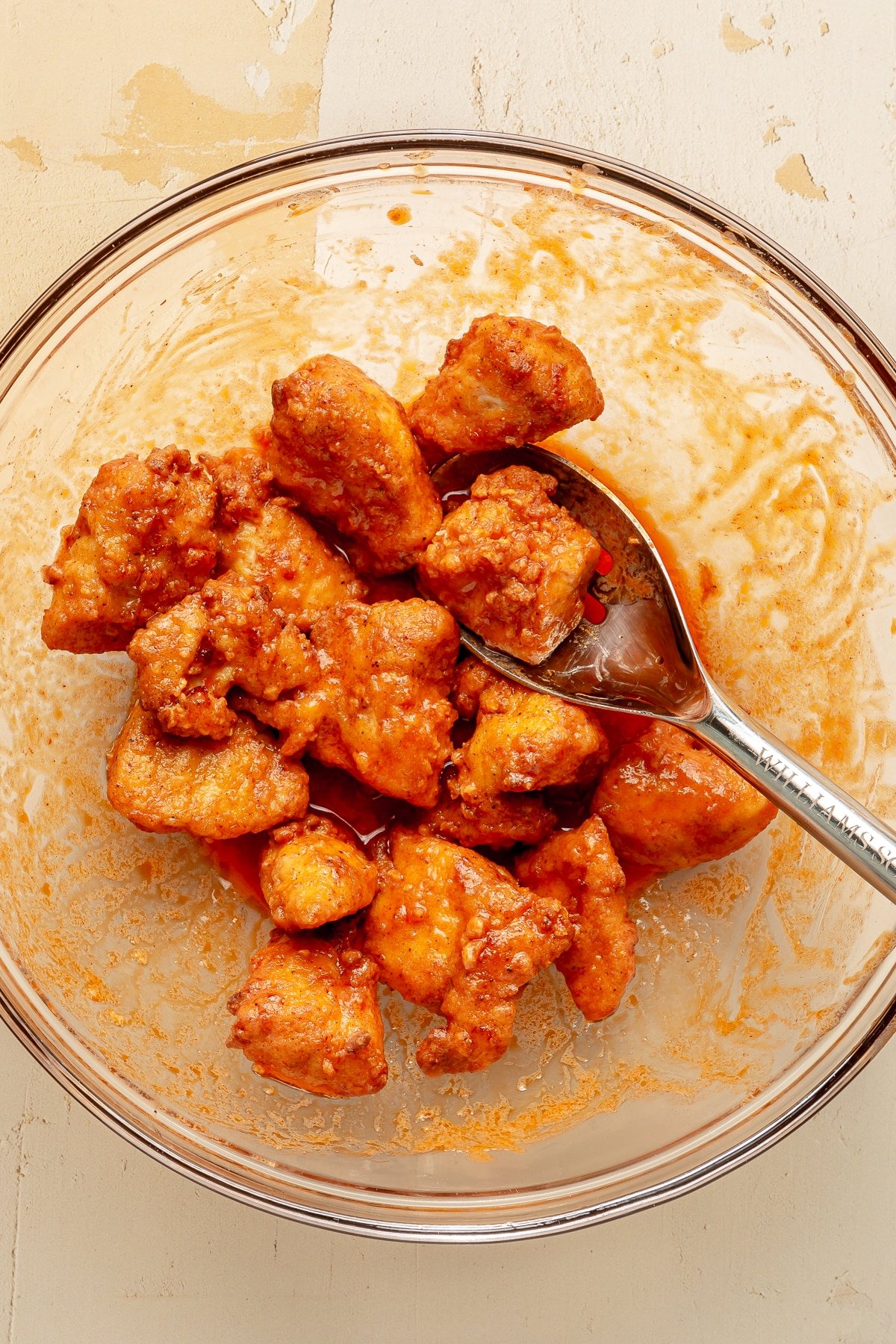 Chicken bites are shown being tossed in buffalo sauce with a metal spoon.