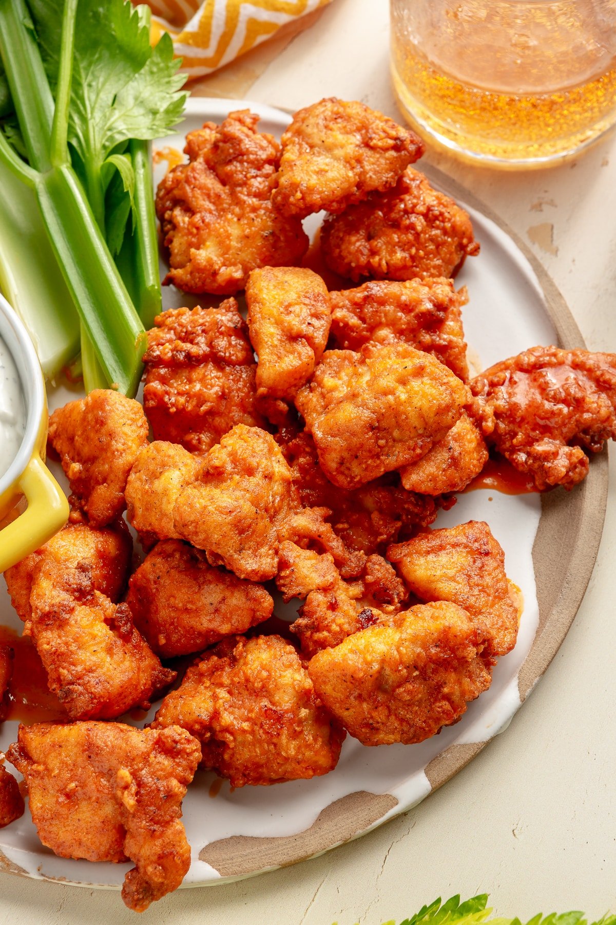 Buffalo chicken bites sit on a serving plate next to a side of blue cheese dip. Pieces of celery sit to the side.