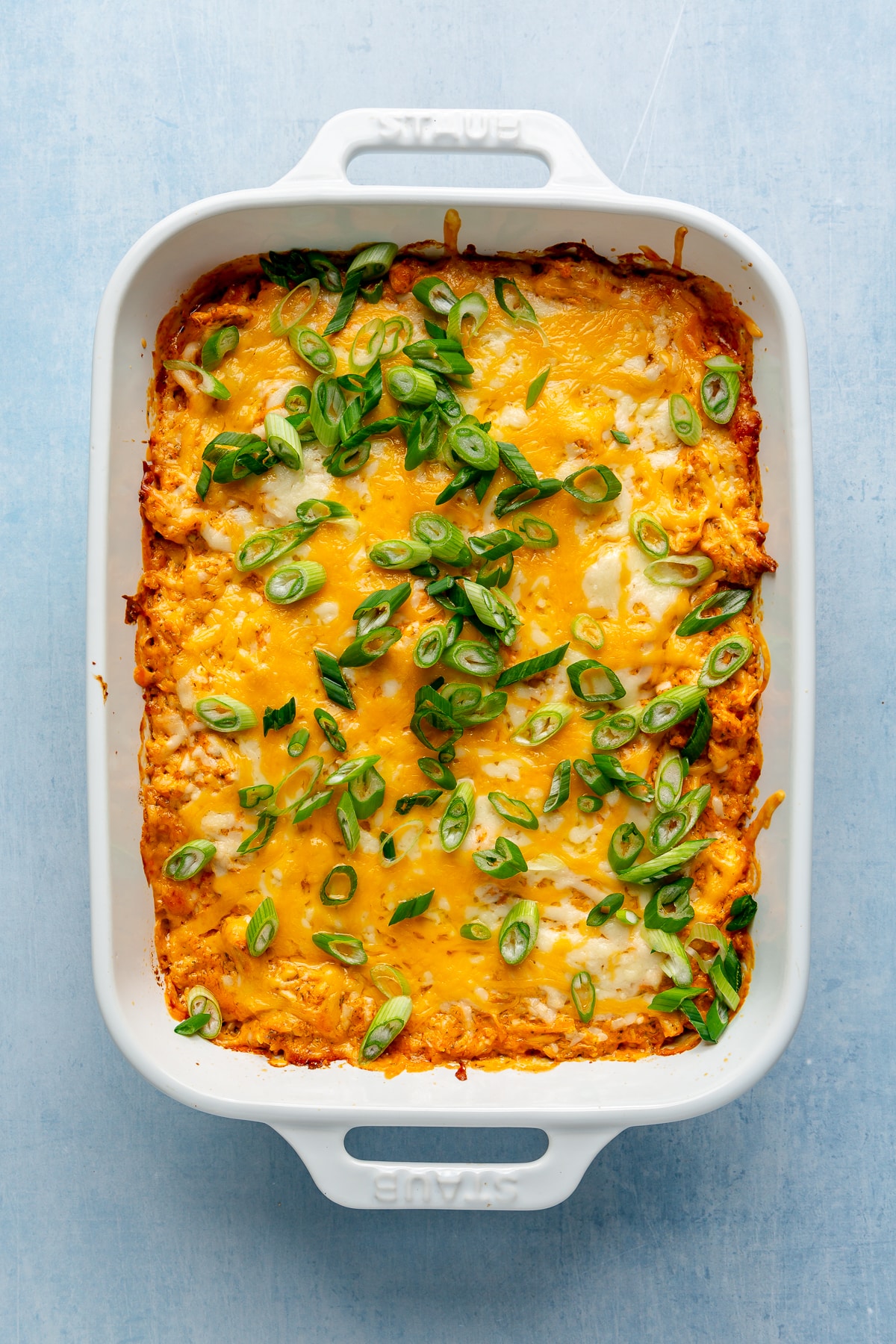 Top view of hot buffalo chicken dip topped with melted cheese and green onions in a 9x13 baking dish.