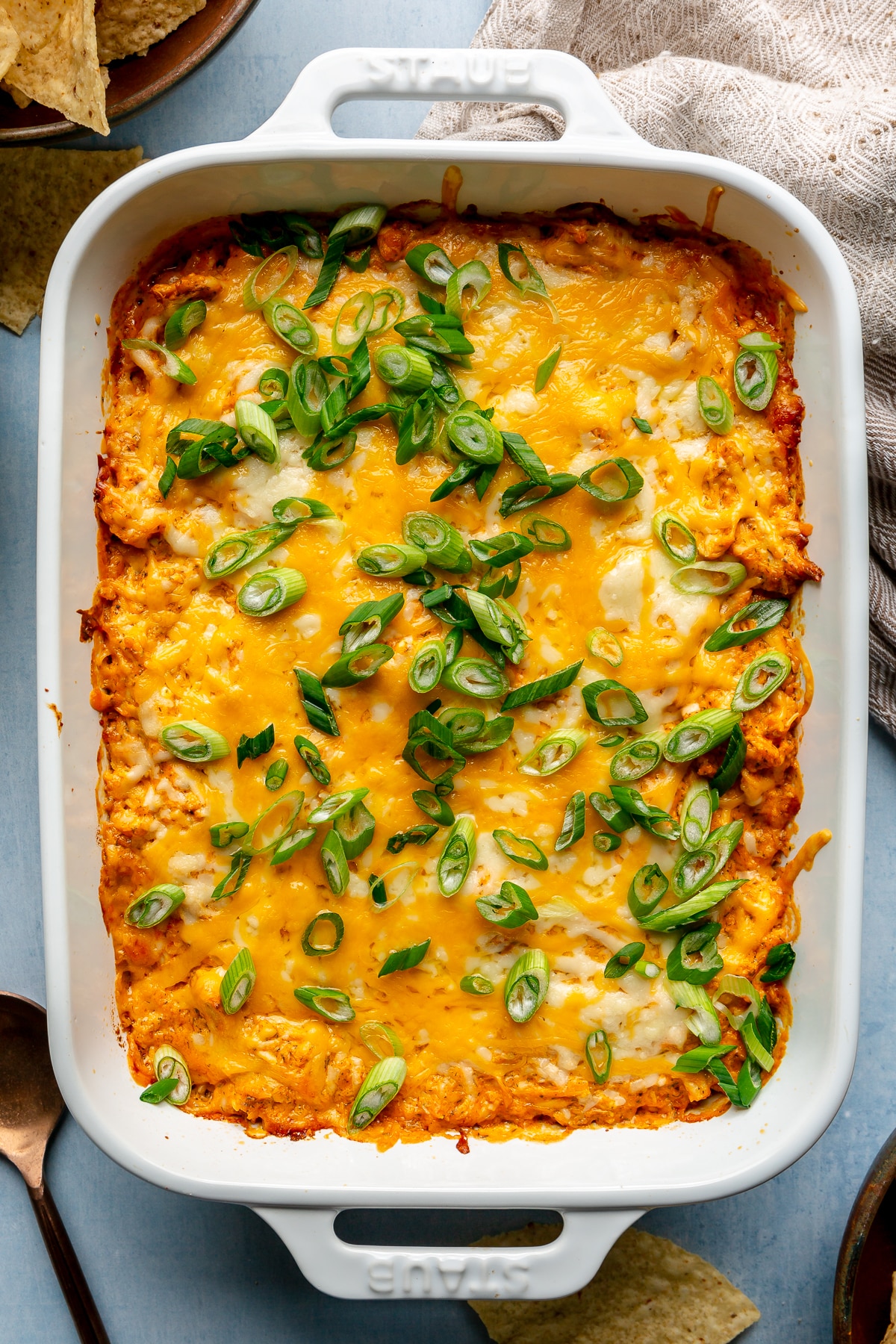 A casserole dish of buffalo chicken dip topped with melted shredded cheese and sliced green onions.