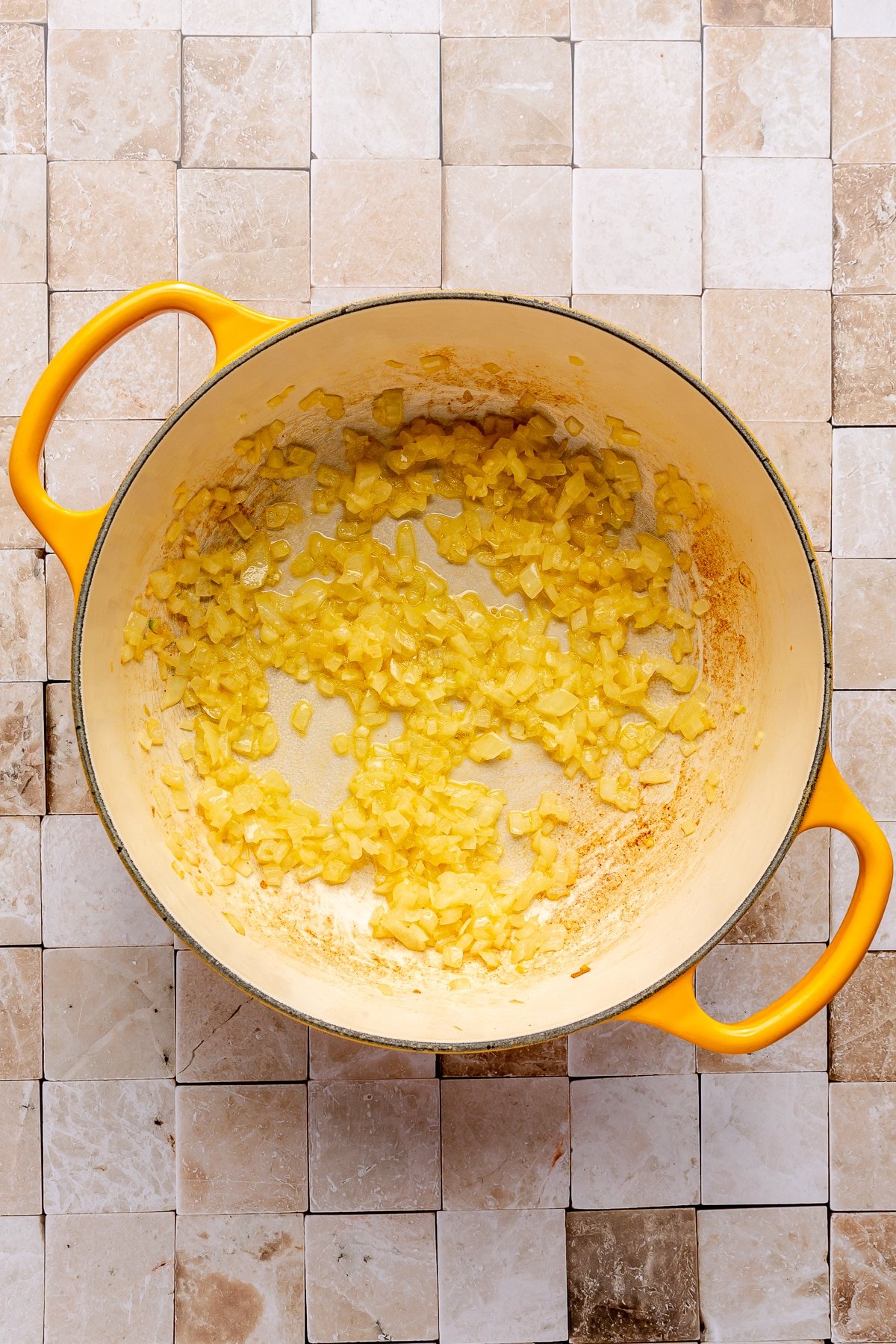 Diced onion and several other ingredients sit in the bottom of a pot with yellow handles.