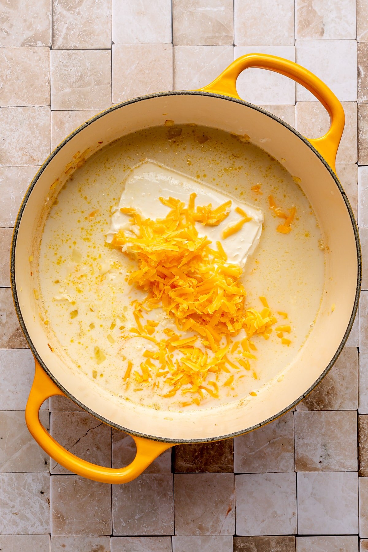 Shredded cheddar cheese, a block of cream cheese, and a cream colored liquid have been added to the pot.