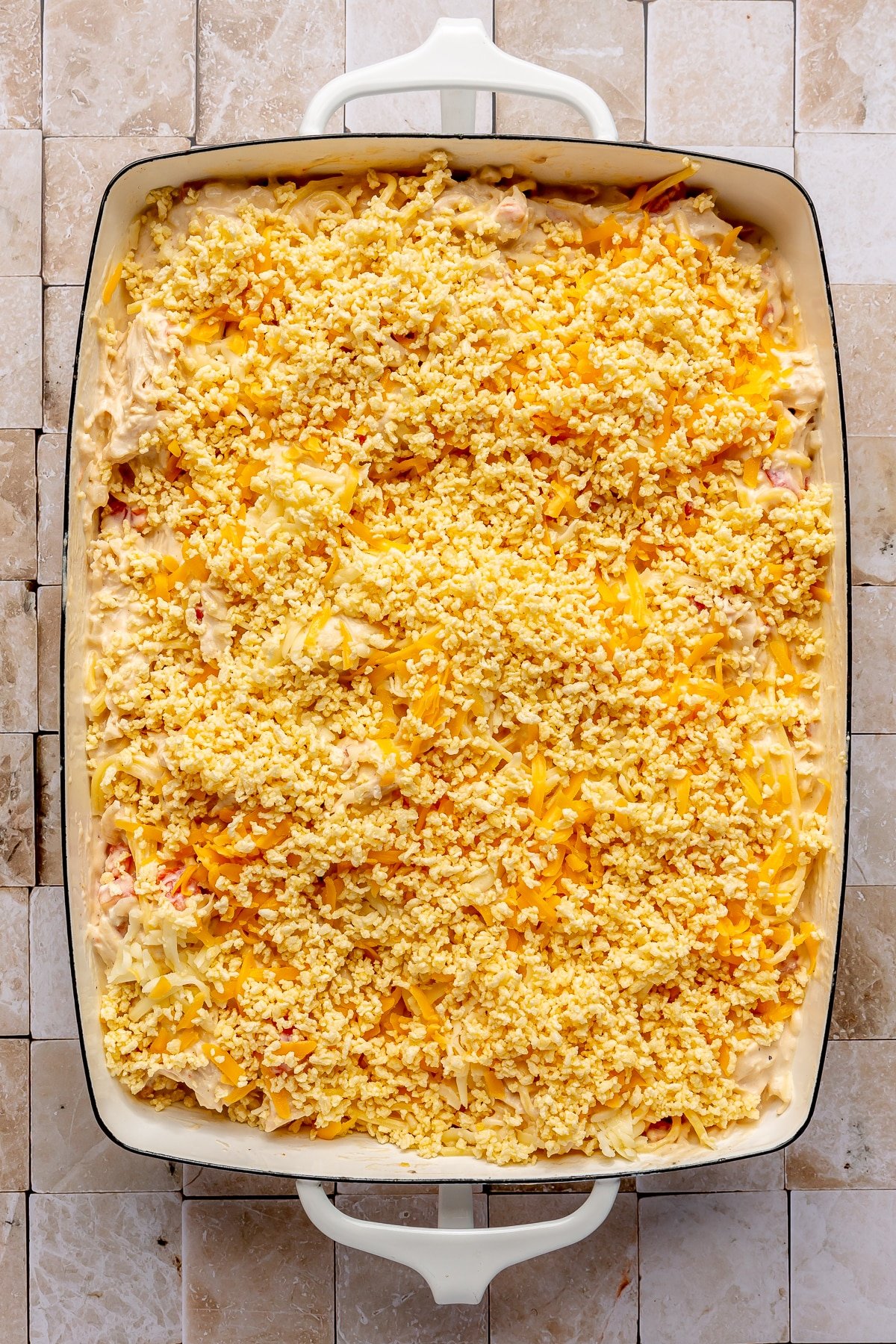 The creamy chicken mixture has been placed in a casserole dish and topped with breadcrumbs and shredded cheddar cheese.