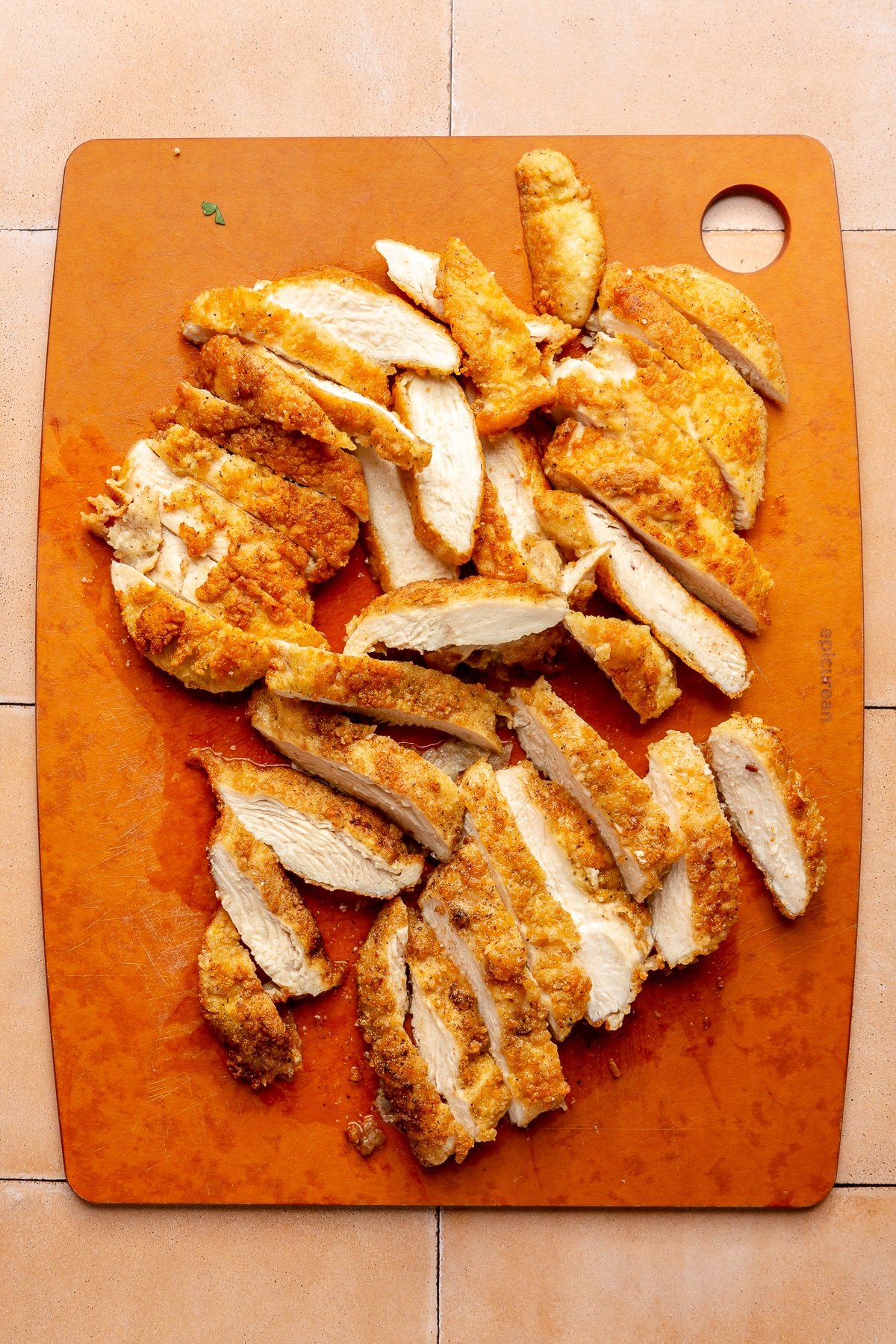 Cut pieces of cooked breaded chicken sit on an orange cutting board.