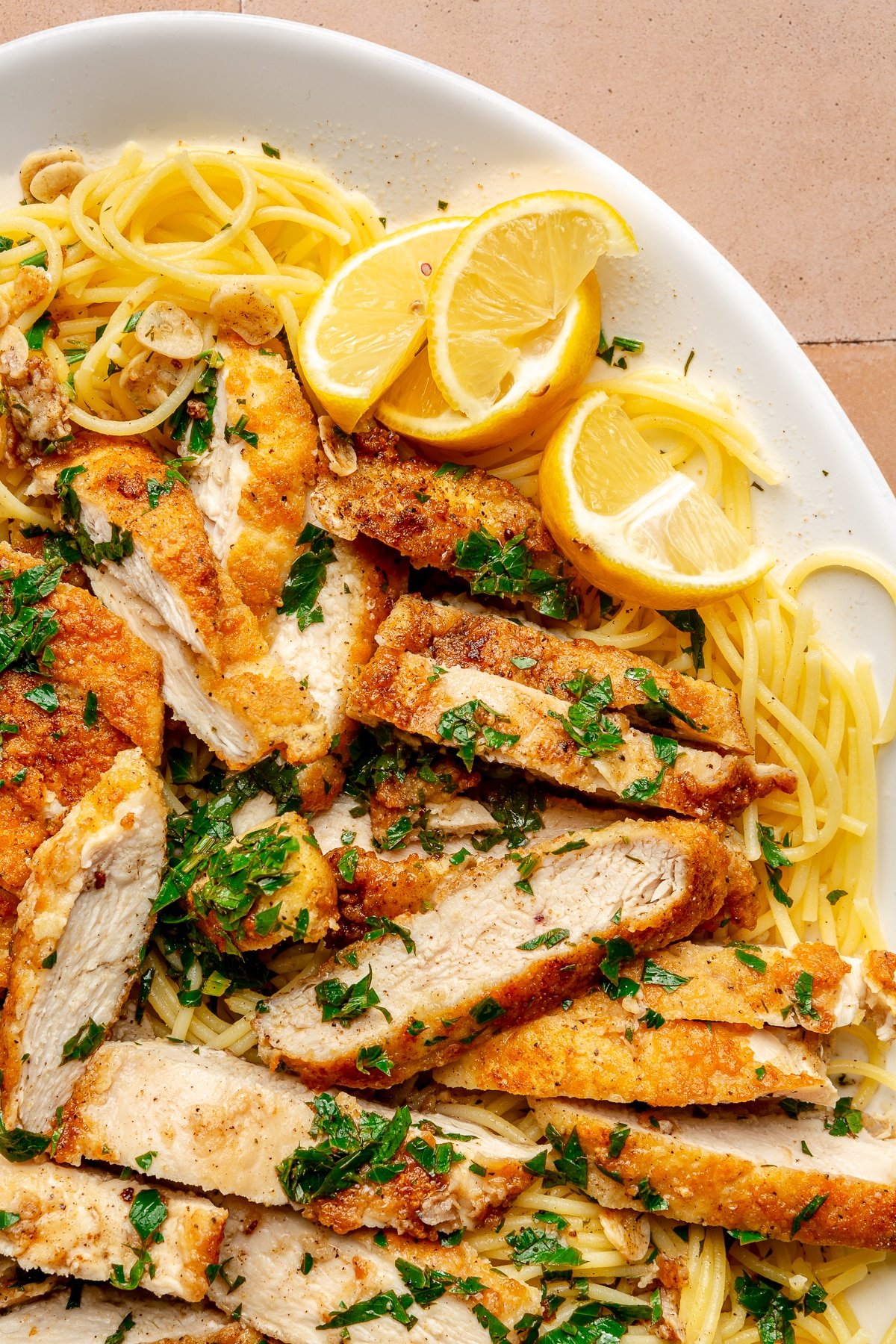 Chicken scampi sits on a bed of spaghetti on a white serving plate. Slices of lemon sit to the side.