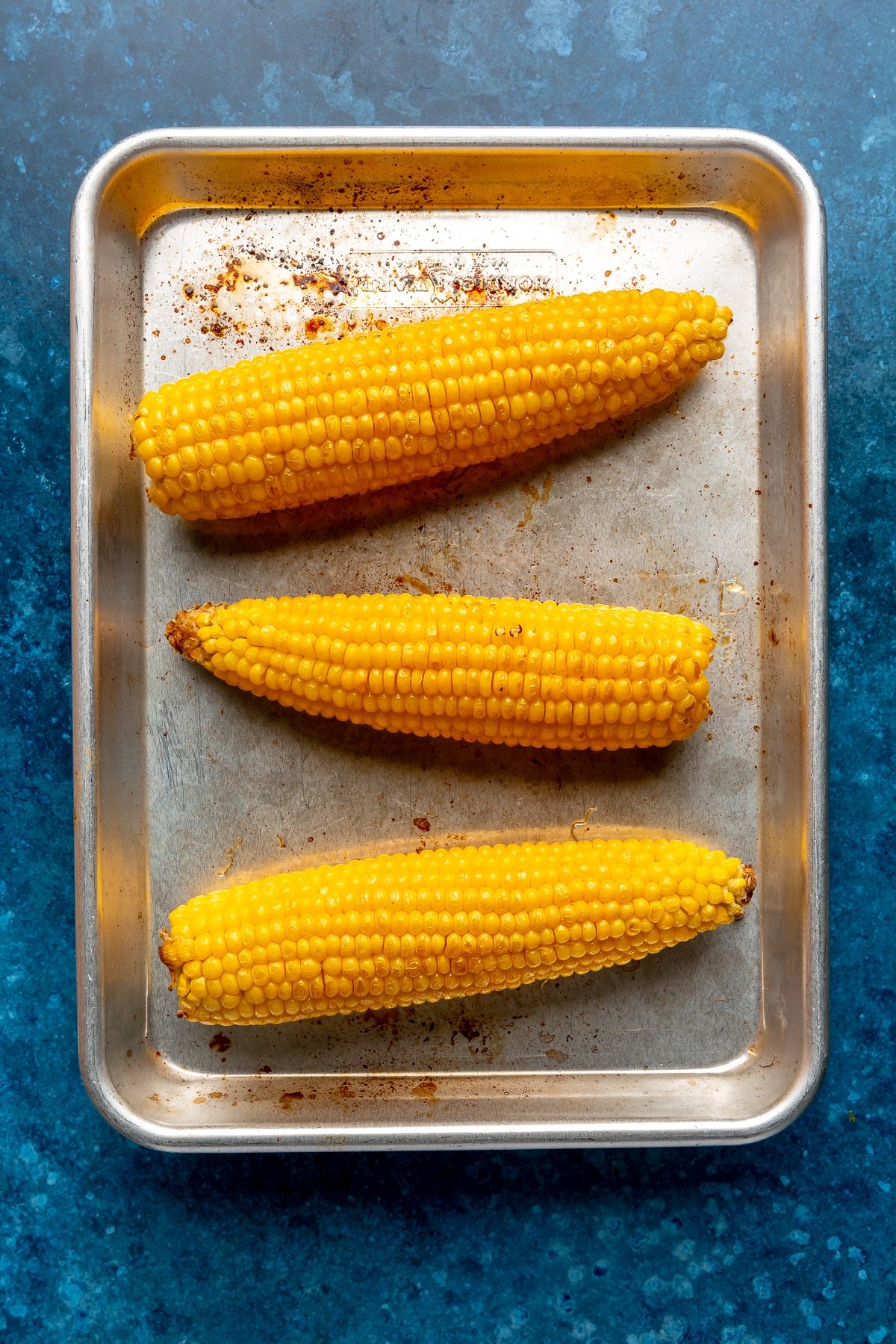 Roasted corn cobs sit on a meral tray.