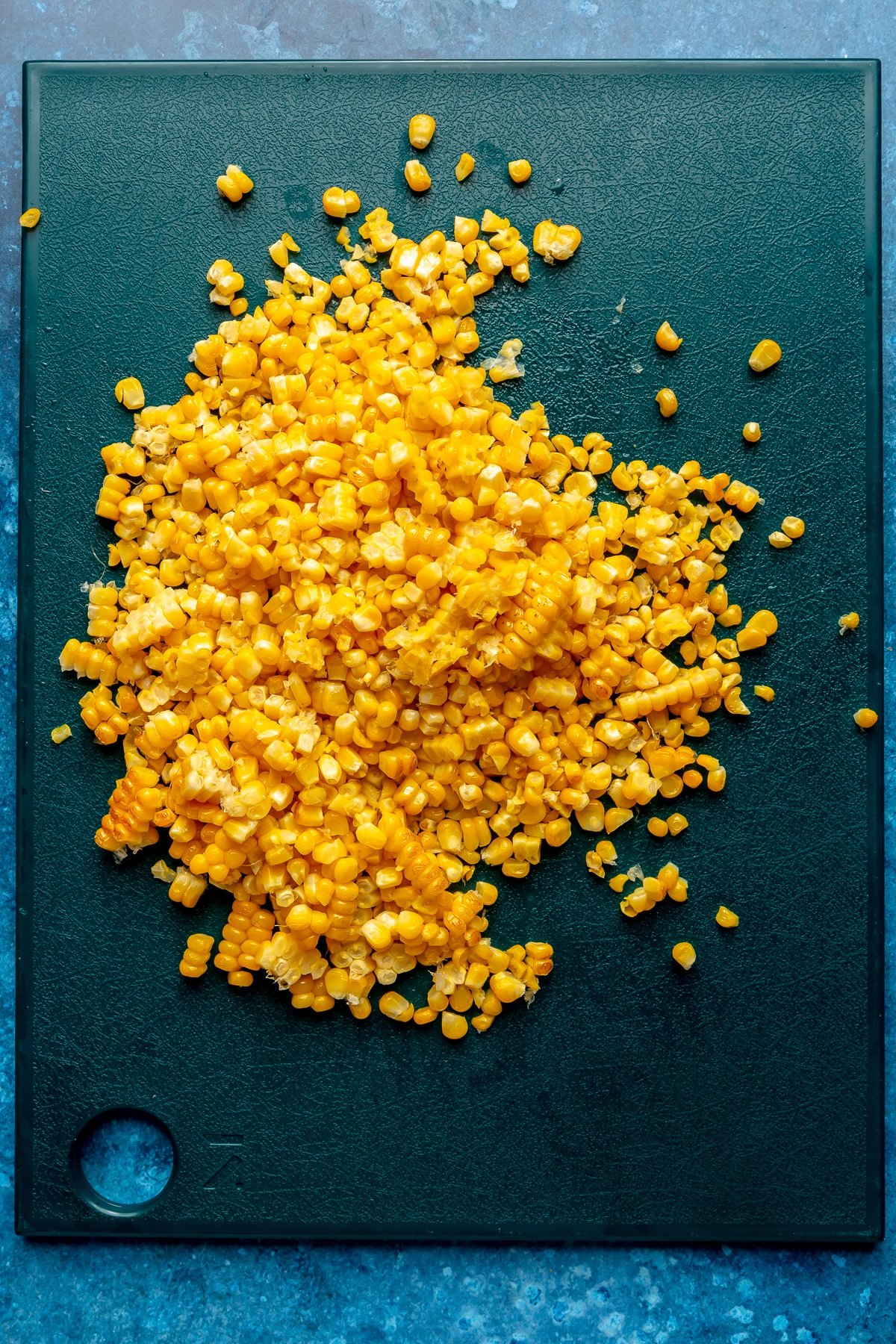 Roasted corn kernels sit on a dark blue cutting board.