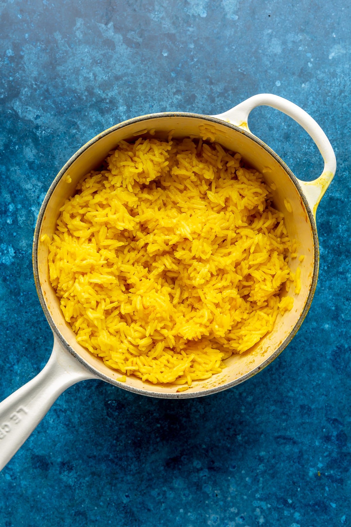 A cooked yellow colored rice sits in a white enameled pot.