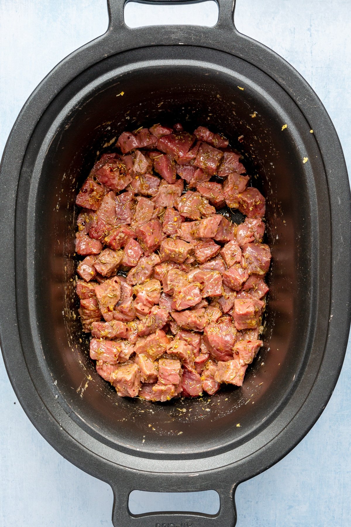 Pieces of beef sit in a slow cooker. They have bene covered in a sauce.