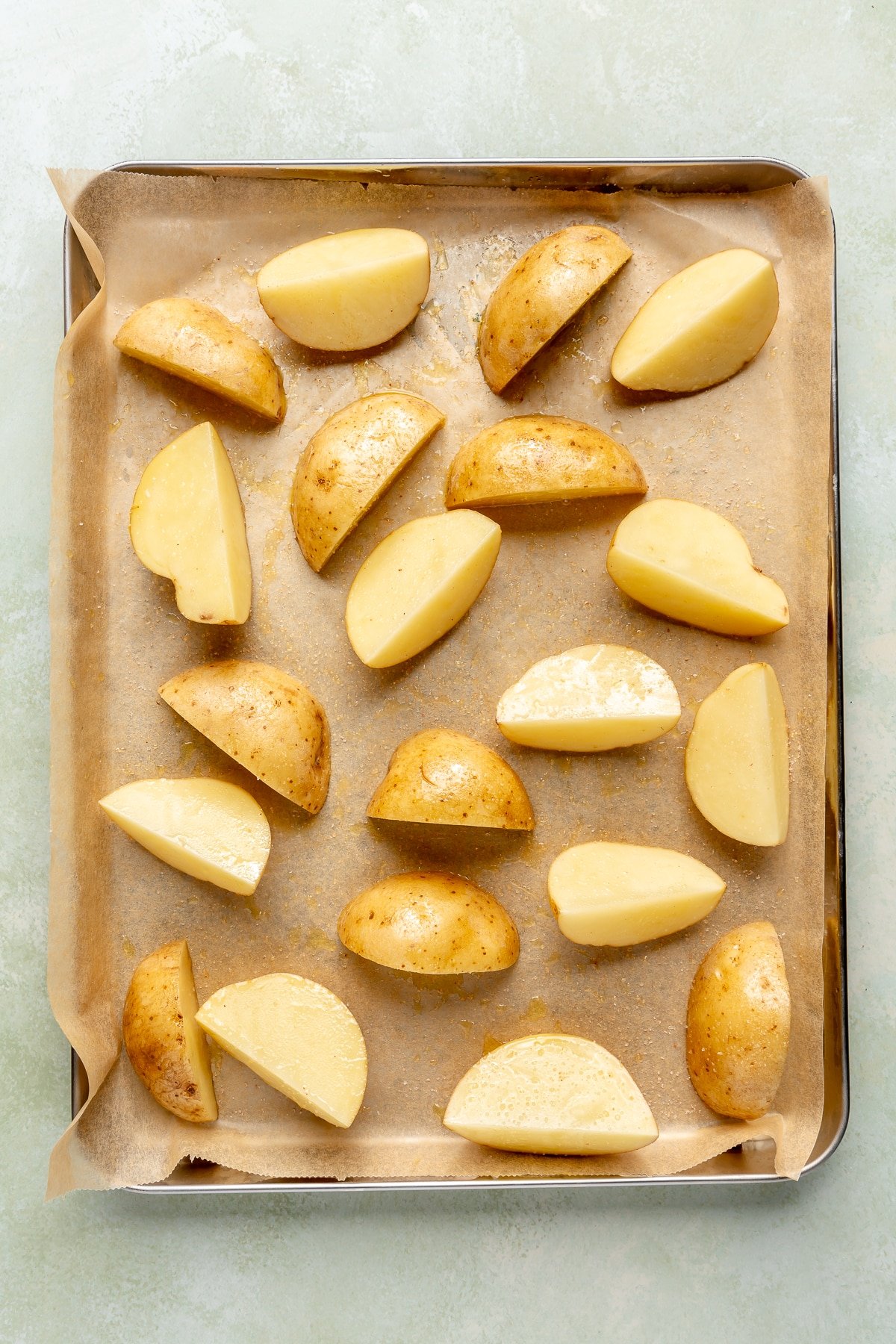 Quartered yellow potatoes have been sprinkled in seasonings and been placed on a parchment lined baking sheet.