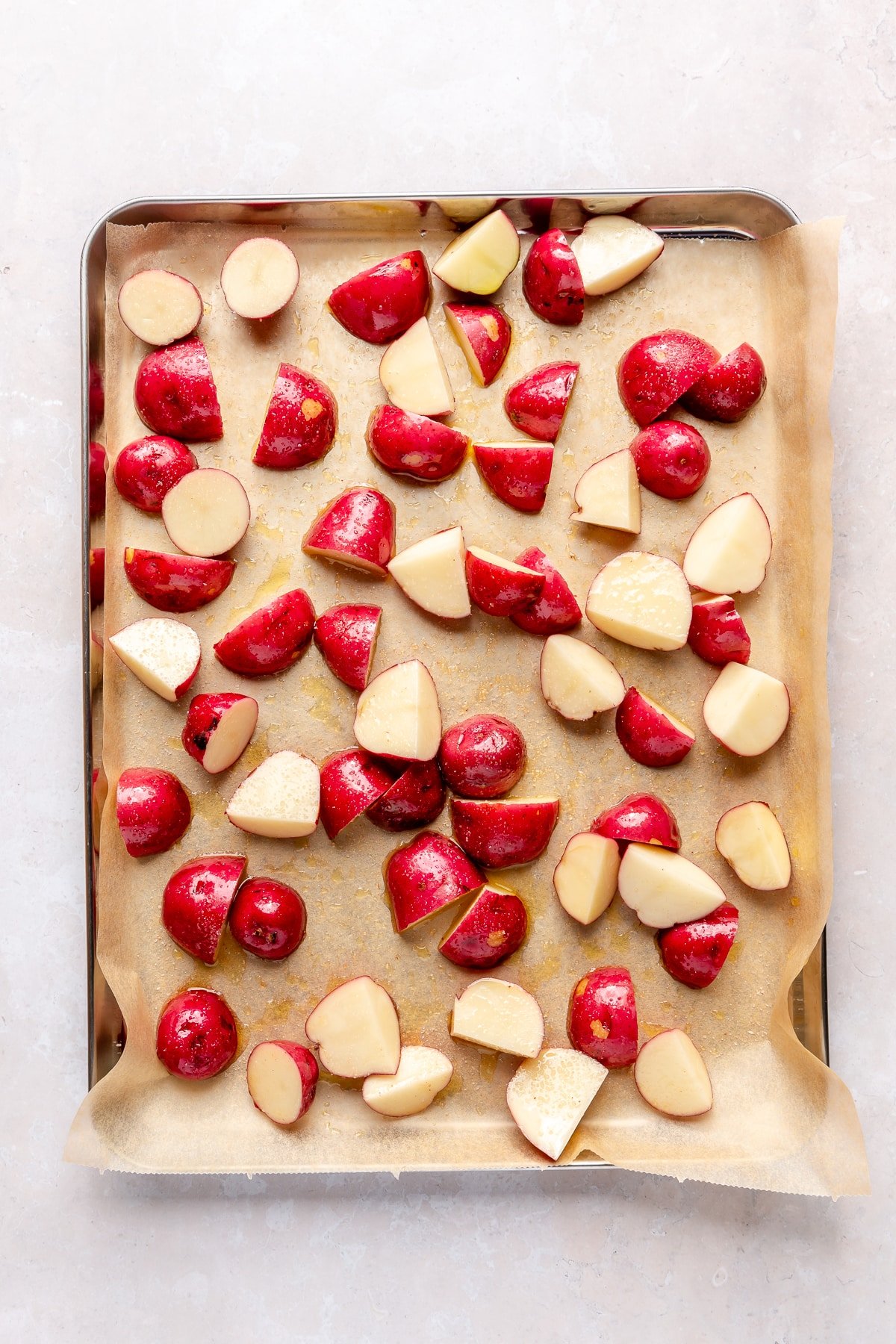 Halved red potatoes sit on a parchment lined baking sheet. They have been drizzled with olive oil and salt.