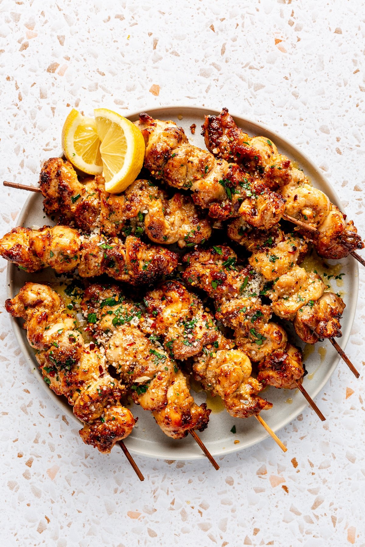 Fully prepared garlic parmesan chicken skewers sit on a grey serving plate. Lemon slices sit to the side.