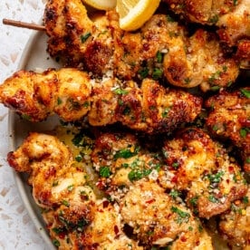 Fully prepared garlic parmesan chicken skewers sit on a grey serving plate. Lemon slices sit to the side.