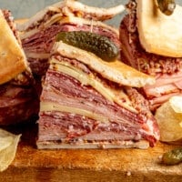 Fully prepared muffaletta sandwiches sit on a wooden chopping block.