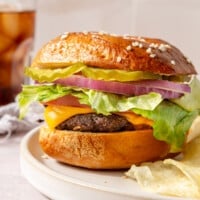 A fully prepared air fryer burger, consisting of lettuce, sliced tomato, melted cheese, pickles, and purple onions, sit on a white plate.